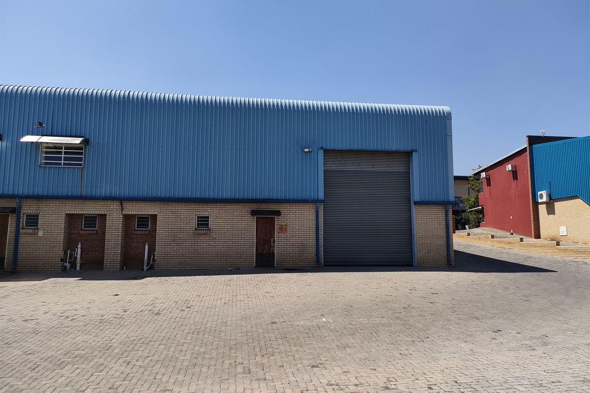 Industrial warehouse exterior featuring a large roller shutter door, face brick facade, and blue corrugated metal cladding with a paved driveway.