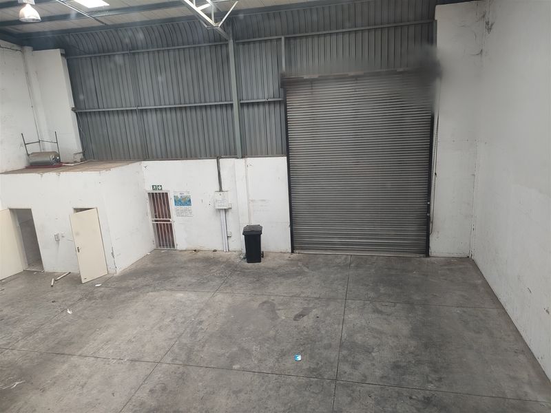 Spacious industrial warehouse unit featuring high ceilings, a large roller shutter door, concrete flooring, and a secure pedestrian entrance.