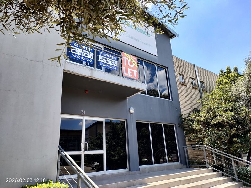 Front elevation of a commercial industrial building featuring a glass storefront, concrete entrance stairs, and a balcony area.