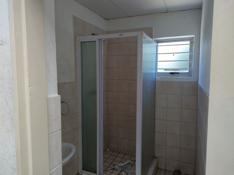 A compact bathroom featuring a shower enclosure, tiled walls and flooring, and a louvered window, currently in need of cosmetic updates.