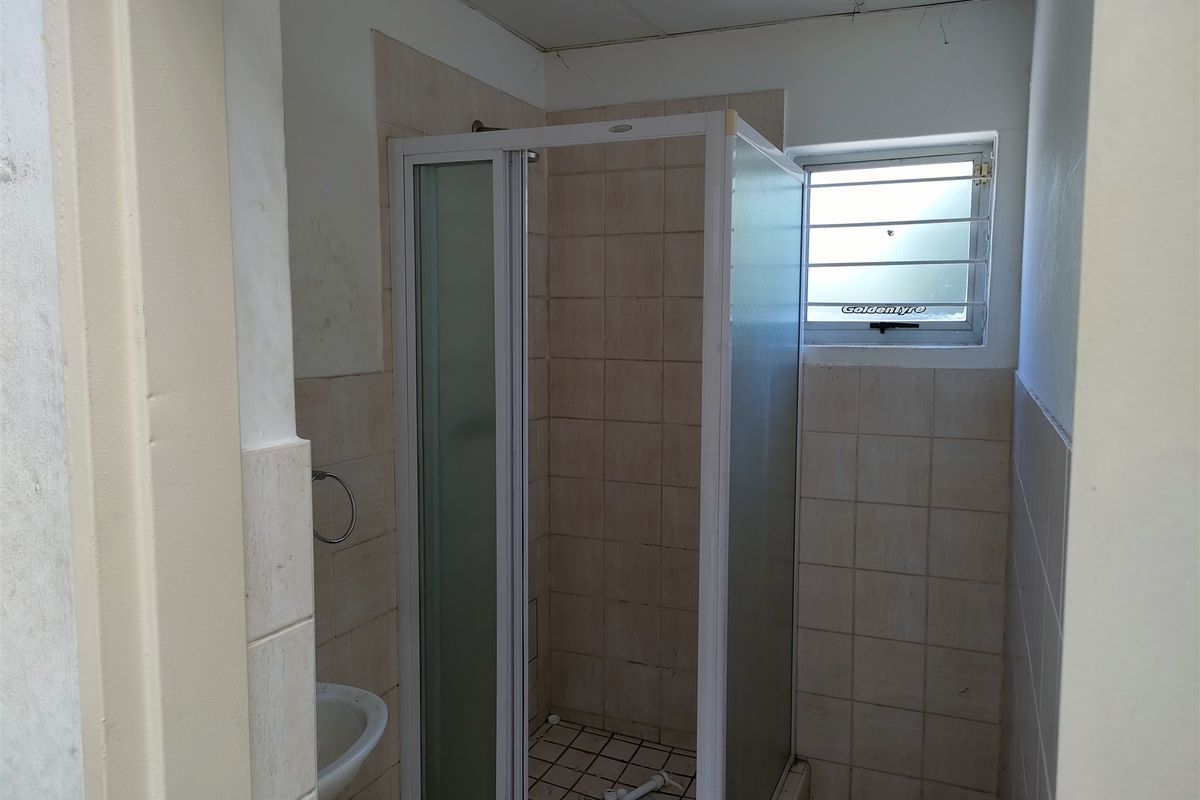 A compact bathroom featuring a shower enclosure, tiled walls and flooring, and a louvered window, currently in need of cosmetic updates.