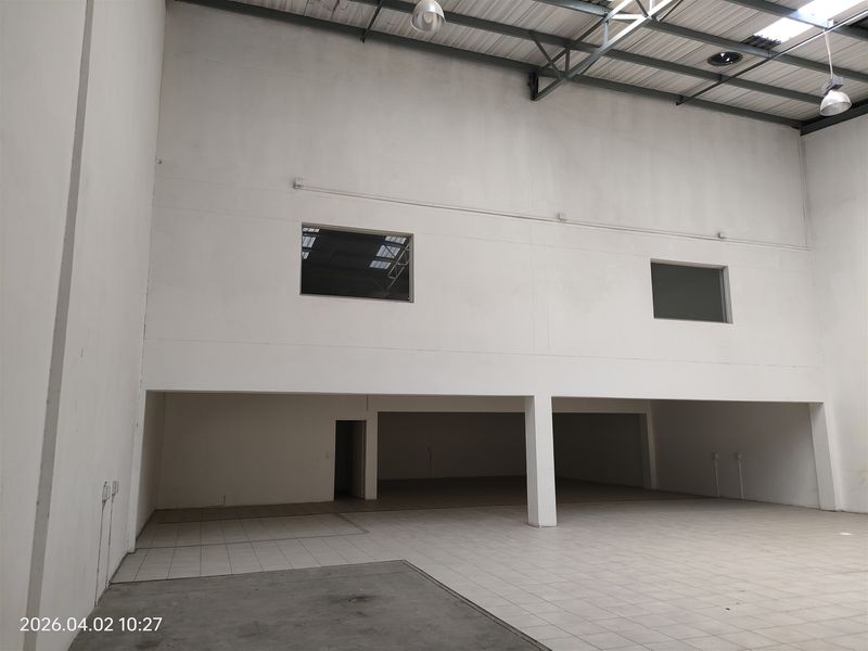 Spacious industrial warehouse unit featuring high ceilings with exposed trusses, tiled flooring, and a mezzanine level with internal windows.