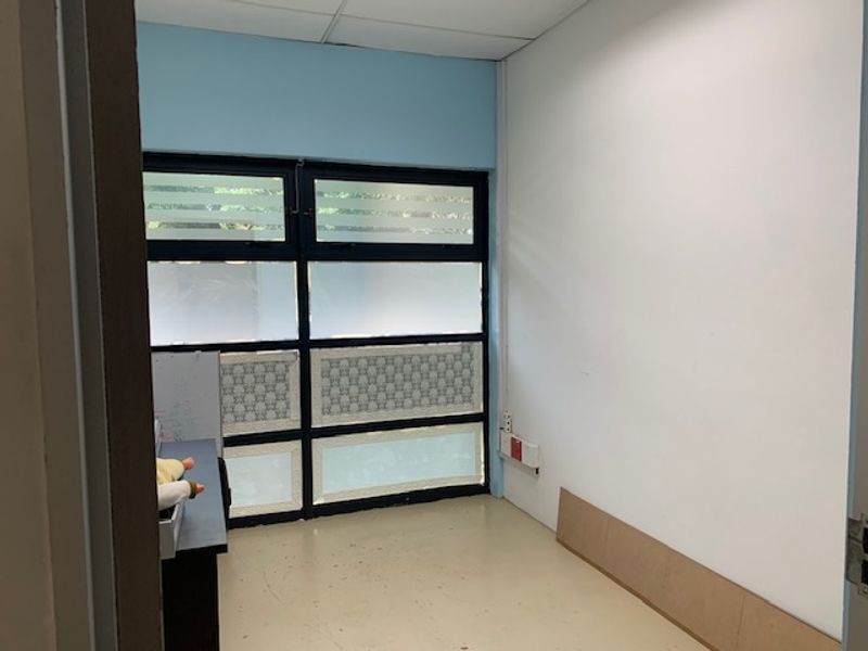 A compact office space featuring a large window with privacy film, drop ceiling, and neutral wall finishes, suitable for a private workspace.