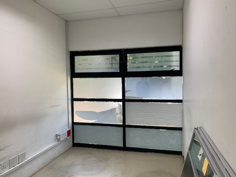 A small, vacant office space featuring a large multi-pane window with frosted privacy film and surface-mounted electrical trunking.