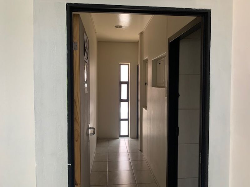 A functional office hallway featuring tiled flooring, recessed lighting, and a narrow vertical window providing natural light.