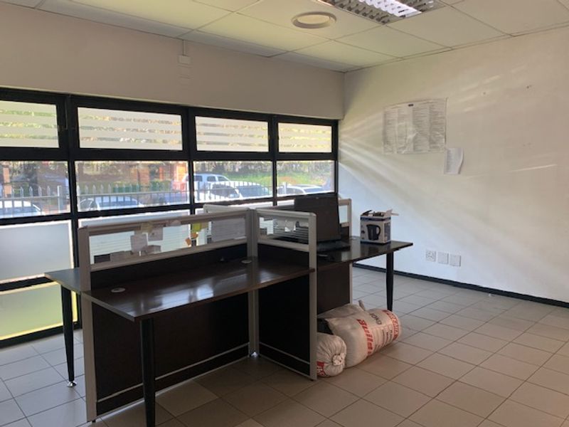 A functional office space featuring large windows, tiled flooring, and integrated desk partitions, providing a bright and practical work environment.