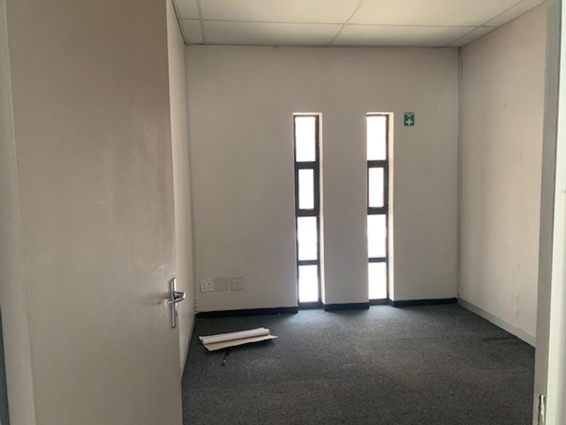 A vacant office space featuring neutral walls, grey carpeting, and two vertical windows providing natural light.