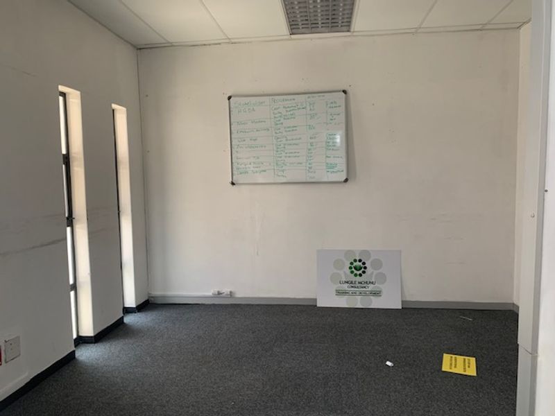 A functional office space featuring a suspended ceiling, grey carpeting, and vertical windows, providing a clean and professional environment for business operations.