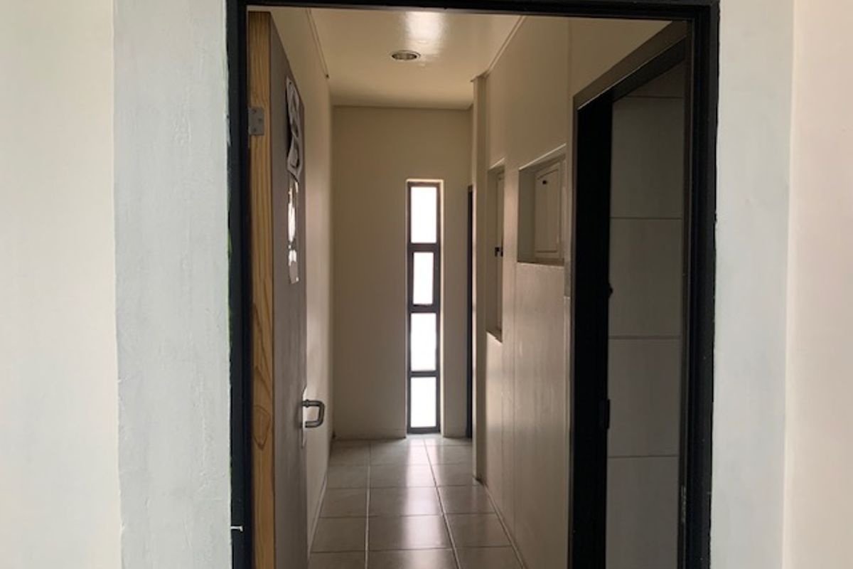 A functional office hallway featuring tiled flooring, recessed lighting, and a narrow vertical window providing natural light.
