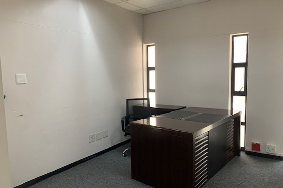 A functional office space featuring grey carpeting, drop ceiling tiles, and two vertical windows providing natural light.