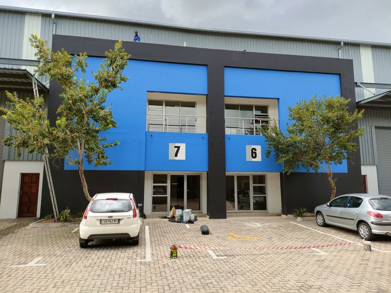 Front elevation of an industrial unit featuring blue and black facade, glass entrance doors, and dedicated paved parking bays.