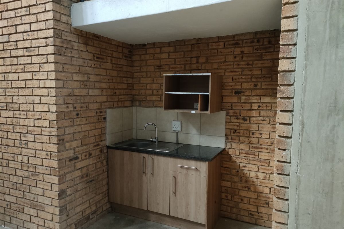 Compact industrial-style kitchenette featuring exposed brick walls, built-in cabinetry with a granite countertop, and a stainless steel sink.