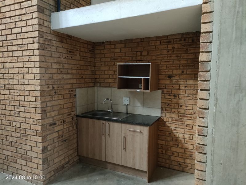 Compact industrial-style kitchenette featuring exposed brick walls, built-in cabinetry with a granite countertop, and a stainless steel sink.