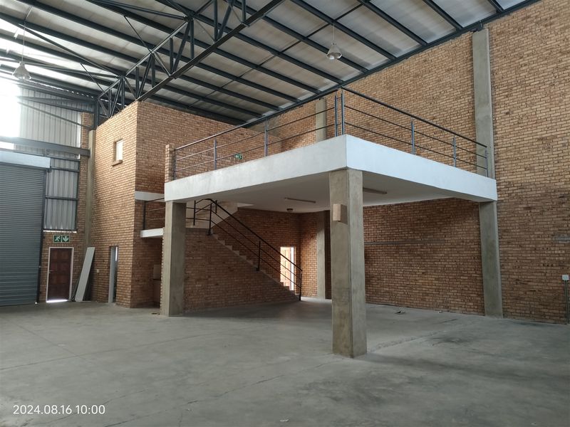 Spacious industrial warehouse unit featuring a mezzanine level, exposed brickwork, high steel roof trusses, and a large roller shutter door for easy access.