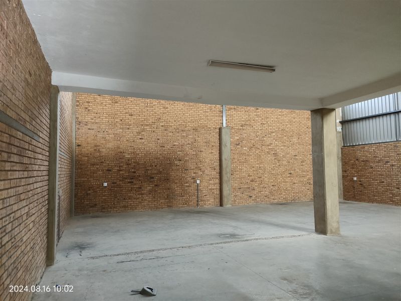Spacious industrial utility area featuring exposed brick walls, concrete flooring, and structural columns, suitable for storage or workshop use.