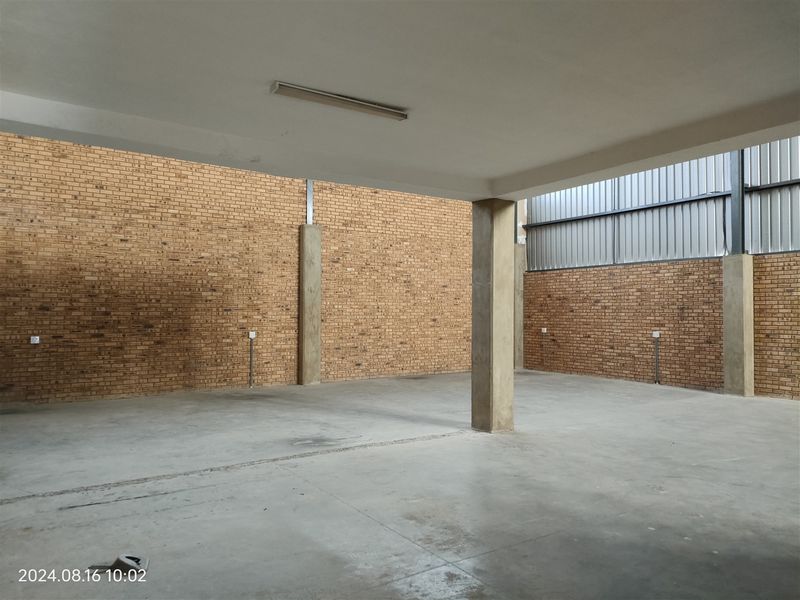 A spacious, open-plan industrial utility area featuring exposed brick walls, concrete flooring, and structural support columns, suitable for storage or workshop use.
