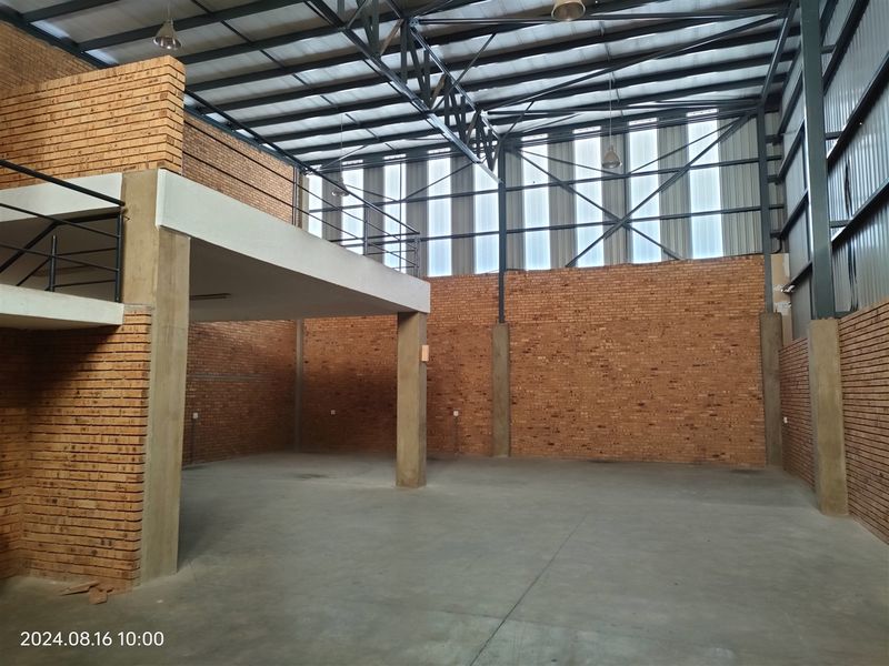 Spacious industrial unit featuring exposed brick walls, concrete flooring, a mezzanine level, and high-clearance steel roof trusses with natural light panels.