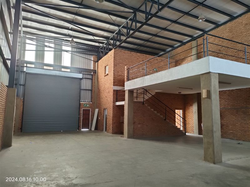 Spacious industrial warehouse unit featuring high ceilings with exposed steel trusses, a large roller shutter door, and a functional mezzanine level with staircase access.