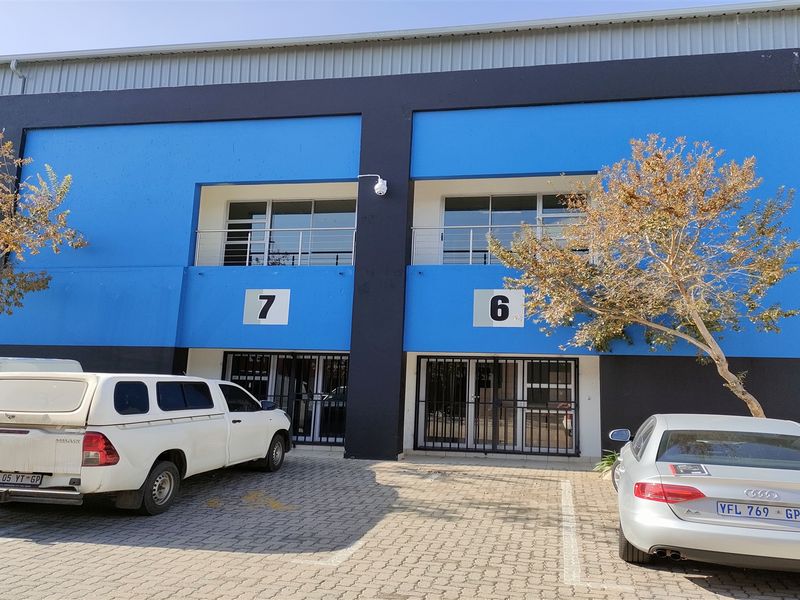 Front elevation of an industrial unit complex featuring blue and black facade, paved parking, and secure ground-floor access points with upper-level balcony access.