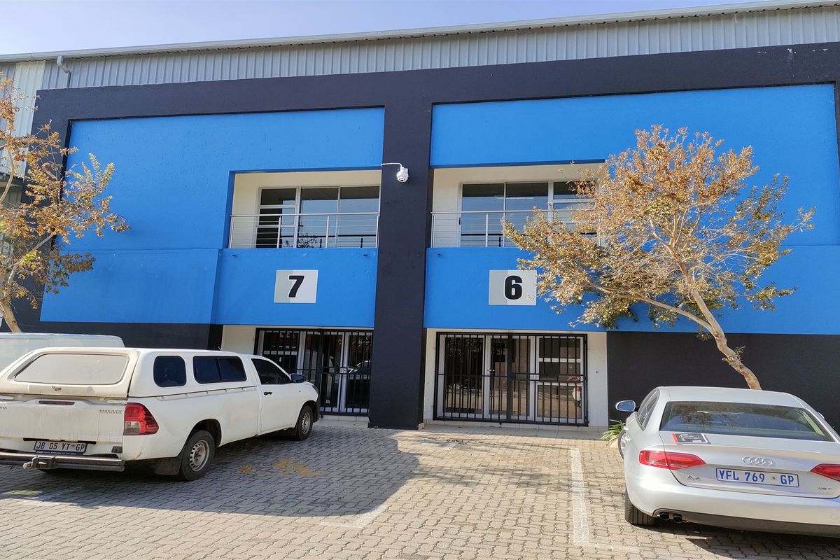 Front elevation of an industrial unit complex featuring blue and black facade, paved parking, and secure ground-floor access points with upper-level balcony access.