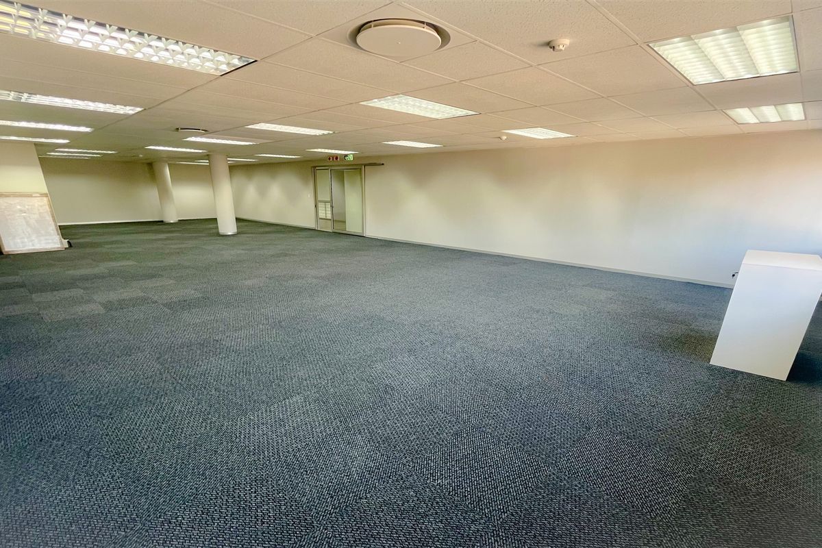A spacious, open-plan office area featuring neutral walls, carpeted flooring, and a suspended ceiling with integrated recessed lighting.