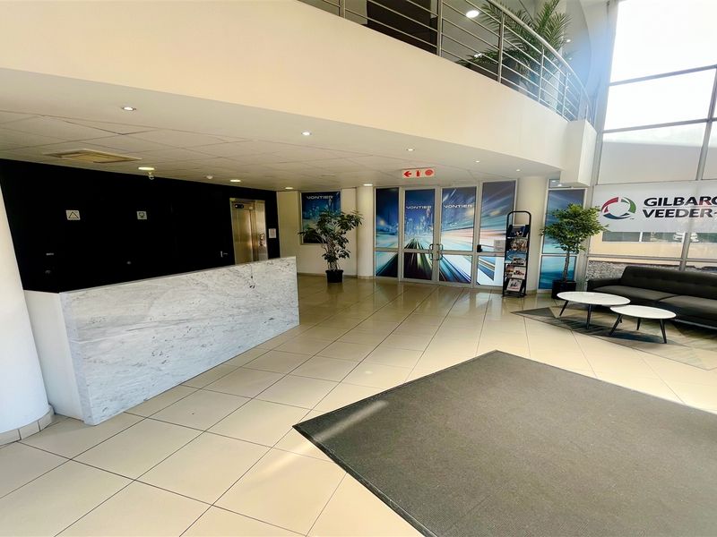 Spacious office building entrance featuring a marble-finish reception desk, double-volume ceiling, large glass windows, and access to an elevator.