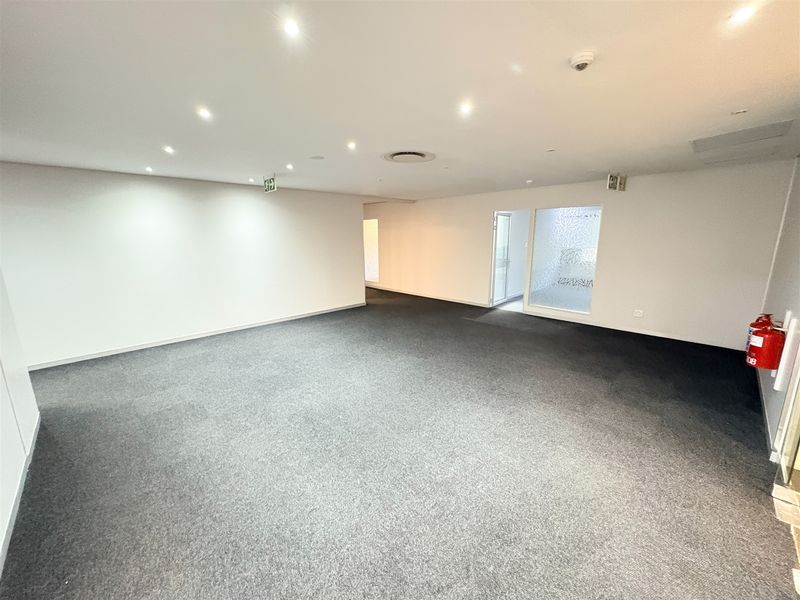 A spacious, empty office area featuring neutral carpet flooring, recessed downlighting, and a frosted glass partition, providing a clean and professional workspace.