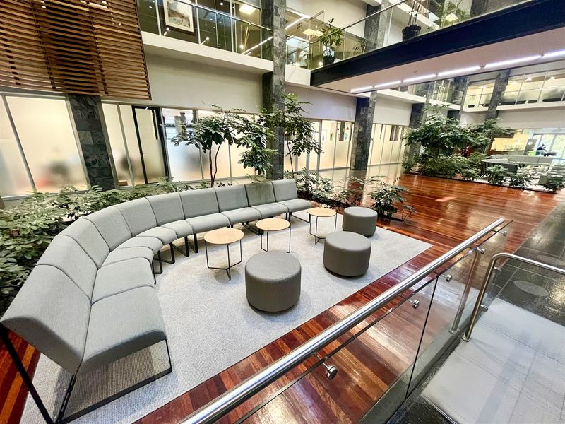 Spacious open-plan office atrium featuring polished hardwood flooring, stone-clad structural columns, and a modern glass balustrade overlooking the lower level.
