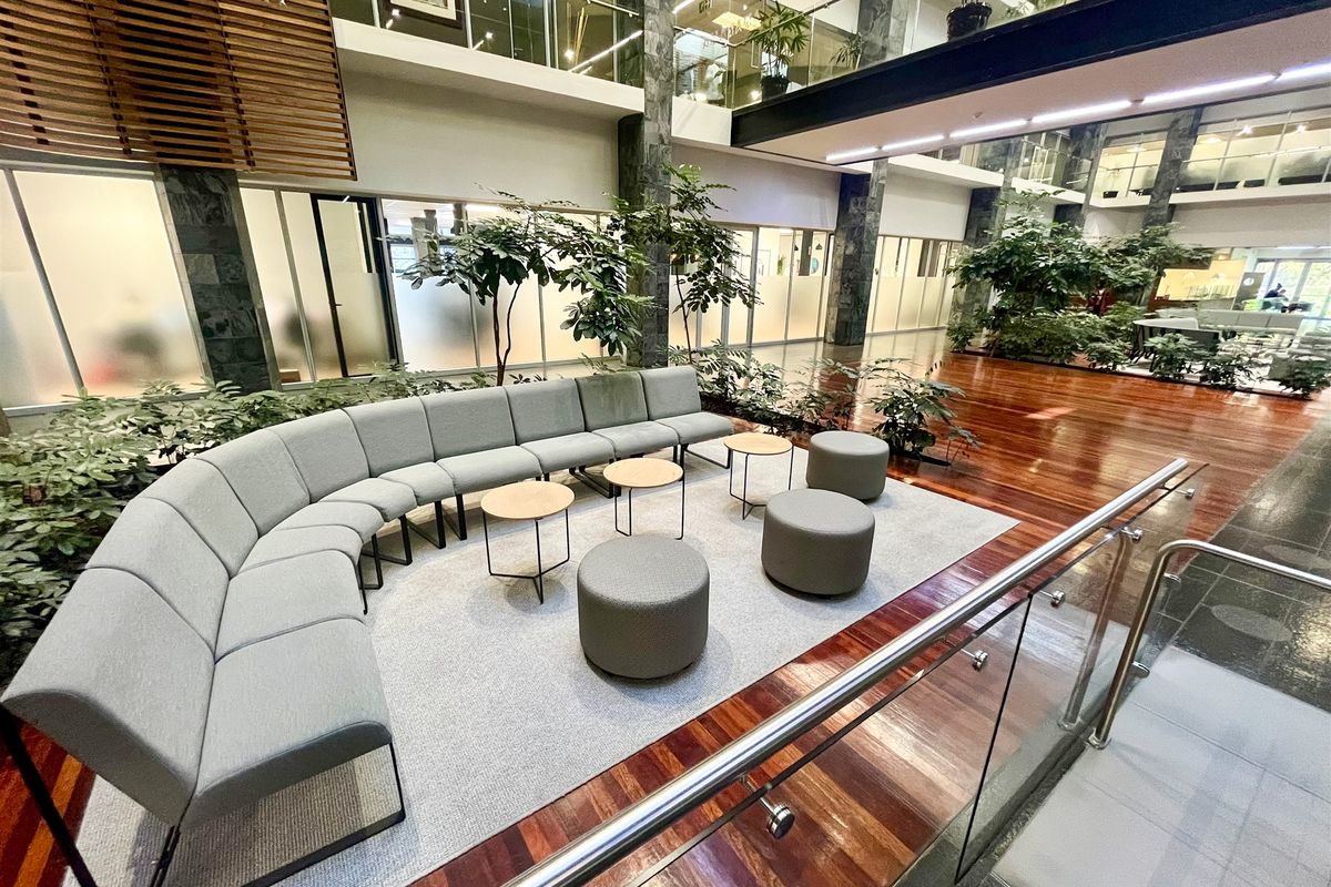 Spacious open-plan office atrium featuring polished hardwood flooring, stone-clad structural columns, and a modern glass balustrade overlooking the lower level.