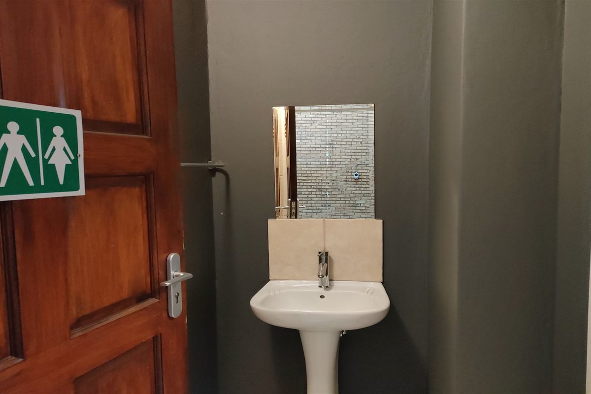 A clean, functional restroom facility featuring a pedestal washbasin, wall-mounted mirror, and tiled splashback.