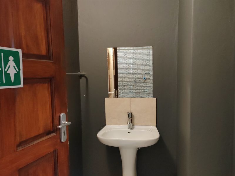 A clean, functional restroom facility featuring a pedestal washbasin, wall-mounted mirror, and tiled splashback.
