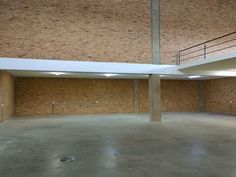 Spacious industrial utility area featuring exposed brick walls, polished concrete flooring, and a functional mezzanine level with metal railing.