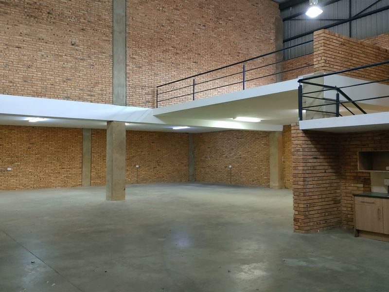 Spacious industrial warehouse unit featuring exposed brick walls, concrete flooring, and a functional mezzanine level with integrated kitchenette cabinetry.