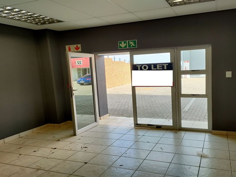 An empty industrial entry space featuring tiled flooring, suspended ceiling with recessed lighting, and an aluminium framed glass door leading to the exterior.