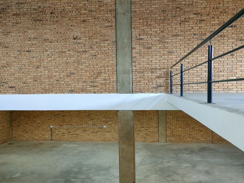 Spacious industrial utility area featuring exposed brick walls, a concrete mezzanine level with metal railing, and durable concrete flooring.