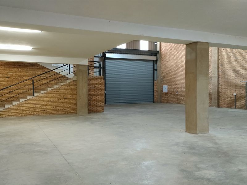 Spacious industrial warehouse unit featuring high ceilings, concrete flooring, exposed brick walls, and a large roller shutter door for easy access.