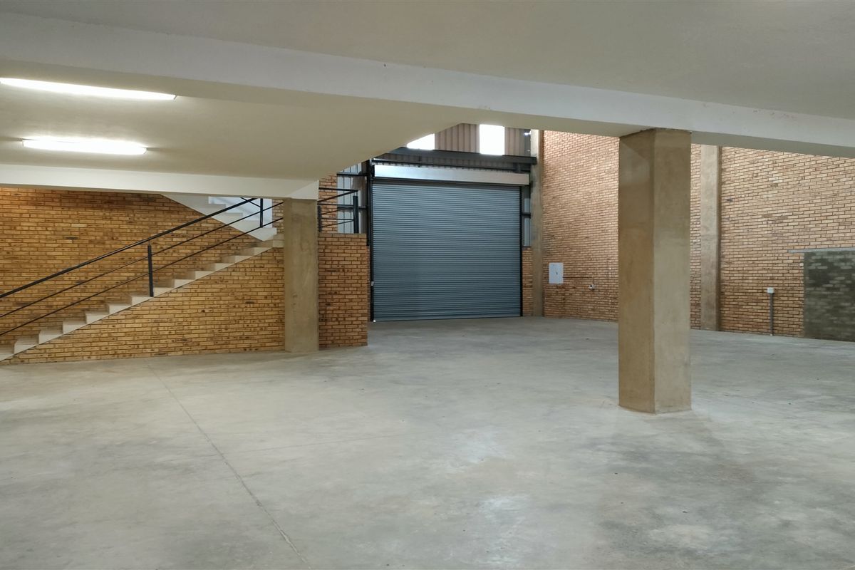 Spacious industrial warehouse unit featuring high ceilings, concrete flooring, exposed brick walls, and a large roller shutter door for easy access.
