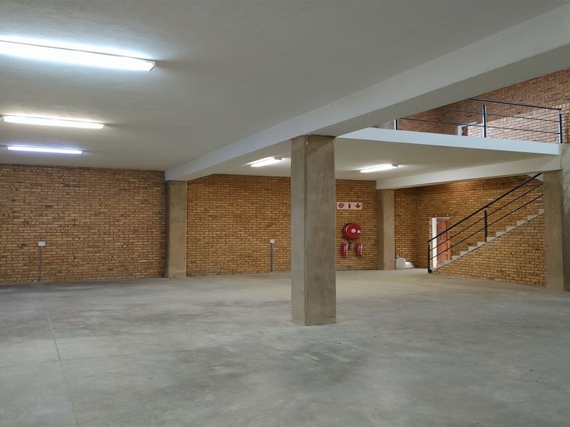 Spacious industrial open-plan area featuring exposed brick walls, polished concrete flooring, a mezzanine level with a metal staircase, and functional overhead lighting.