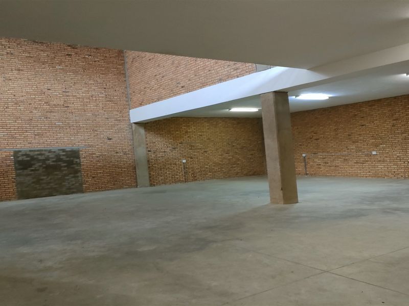Spacious open-plan industrial area featuring exposed brick walls, polished concrete flooring, and functional overhead fluorescent lighting, suitable for various commercial or storage uses.