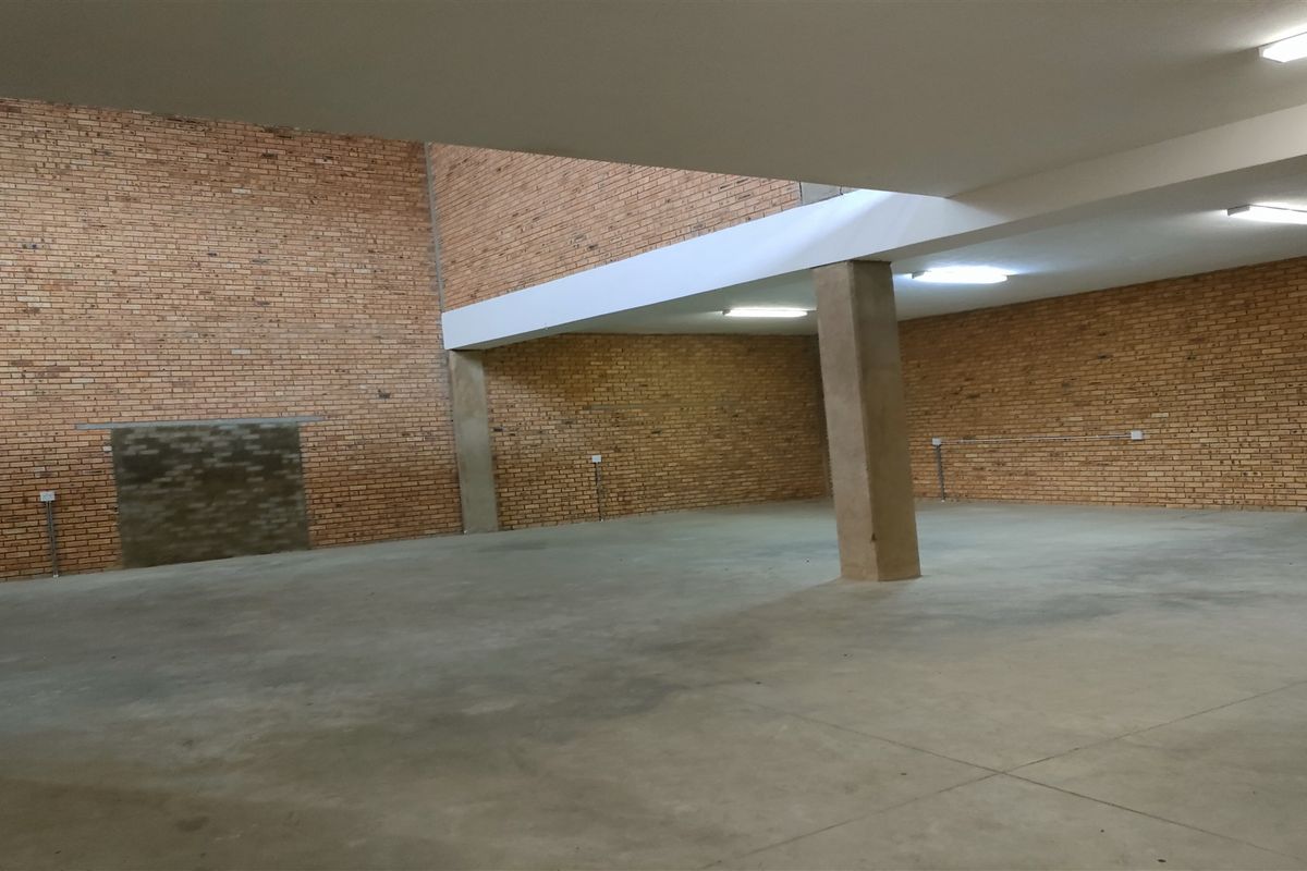 Spacious open-plan industrial area featuring exposed brick walls, polished concrete flooring, and functional overhead fluorescent lighting, suitable for various commercial or storage uses.