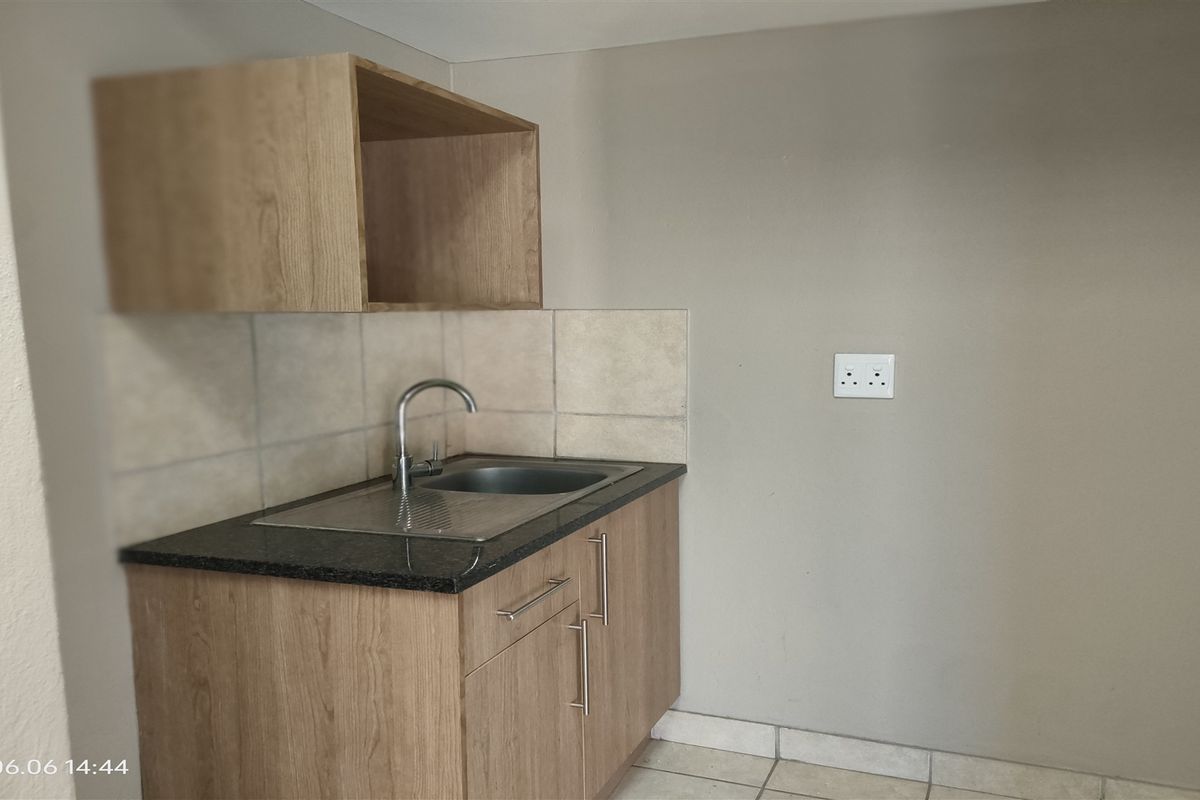 A compact kitchen area featuring built-in wooden cabinetry, a stainless steel sink with a mixer tap, granite countertops, and tiled backsplash.