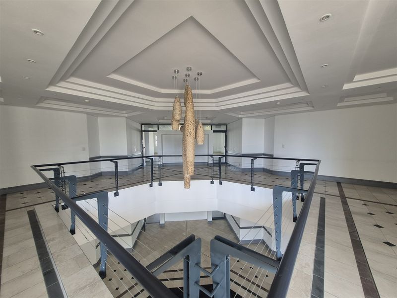 Spacious office building lobby or landing area featuring a tiered ceiling, modern metal balustrades, and neutral tiled flooring.