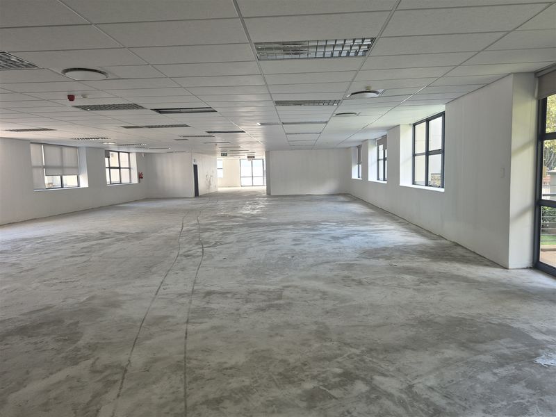 A large, open-plan office space featuring a suspended ceiling, recessed lighting, and expansive windows, currently awaiting final flooring installation.