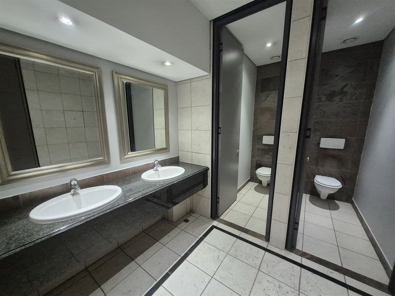 A modern, well-maintained office bathroom featuring a double vanity with granite countertops and two separate toilet cubicles with tiled finishes.