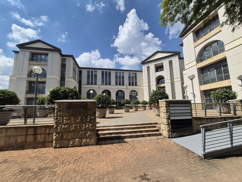 A well-maintained office complex exterior featuring a paved courtyard, stone masonry accents, and modern multi-story architectural design with large arched windows.