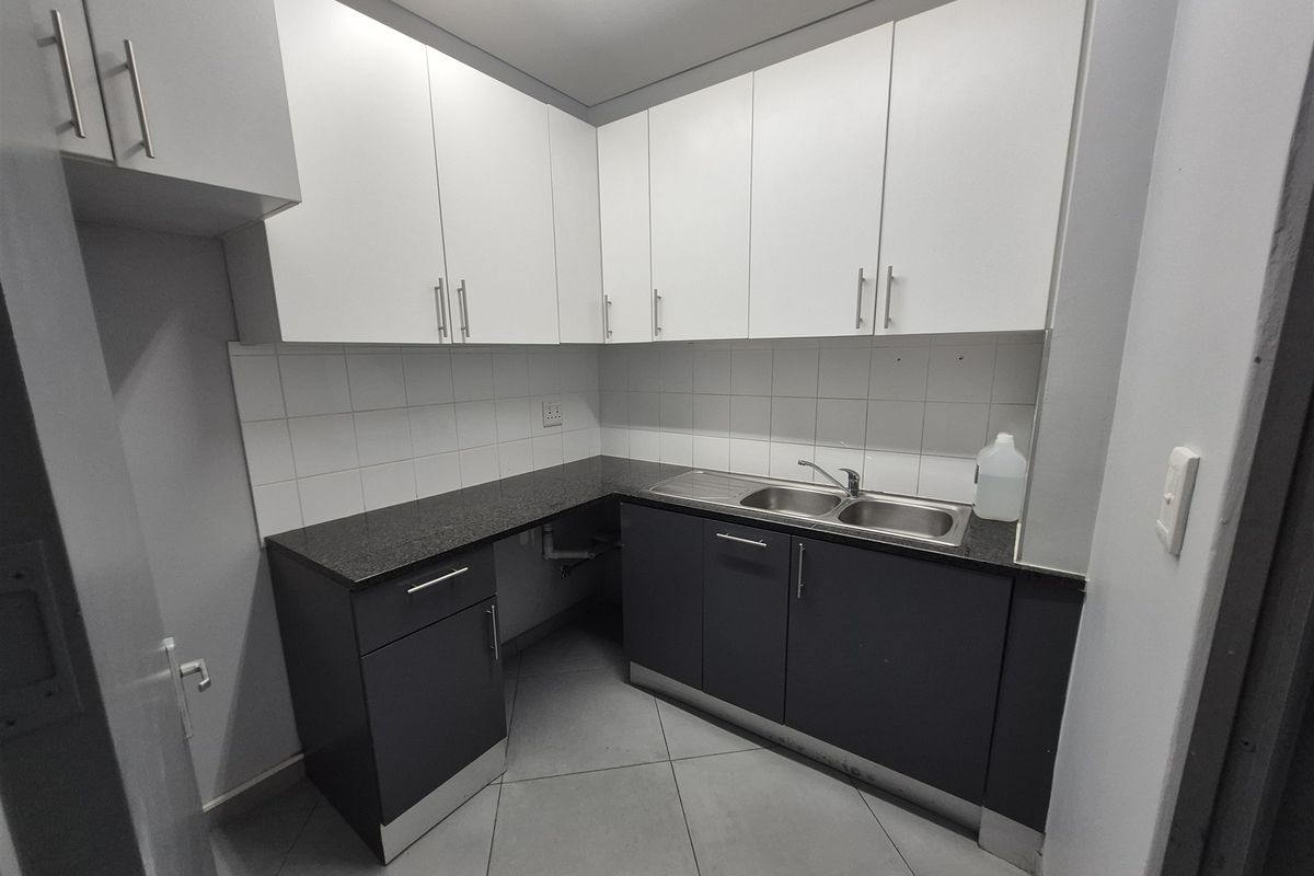 A clean and functional kitchenette featuring modern two-tone cabinetry, granite countertops, a stainless steel double sink, and tiled flooring.