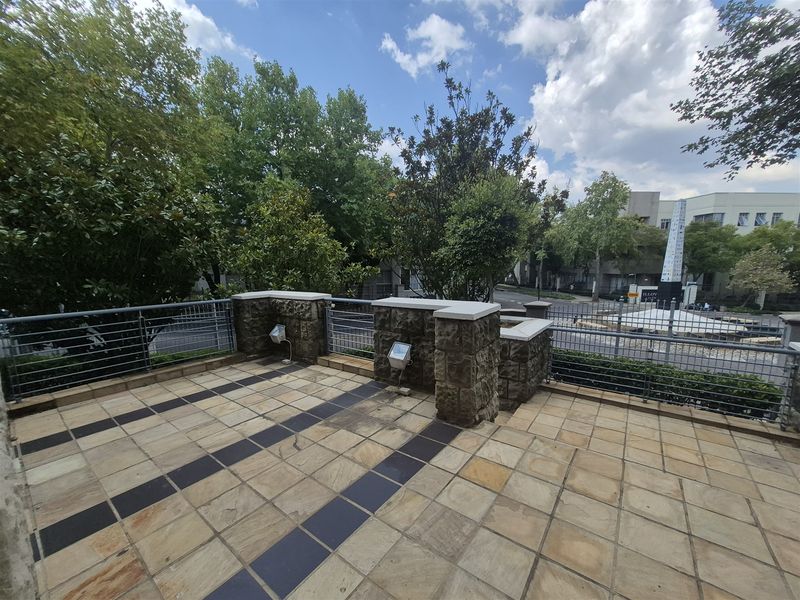 An elevated outdoor patio area featuring stone tile flooring, decorative stone masonry pillars, and metal safety railings overlooking the street.
