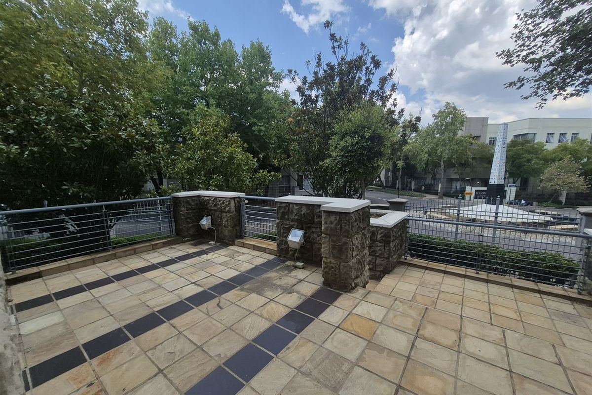 An elevated outdoor patio area featuring stone tile flooring, decorative stone masonry pillars, and metal safety railings overlooking the street.