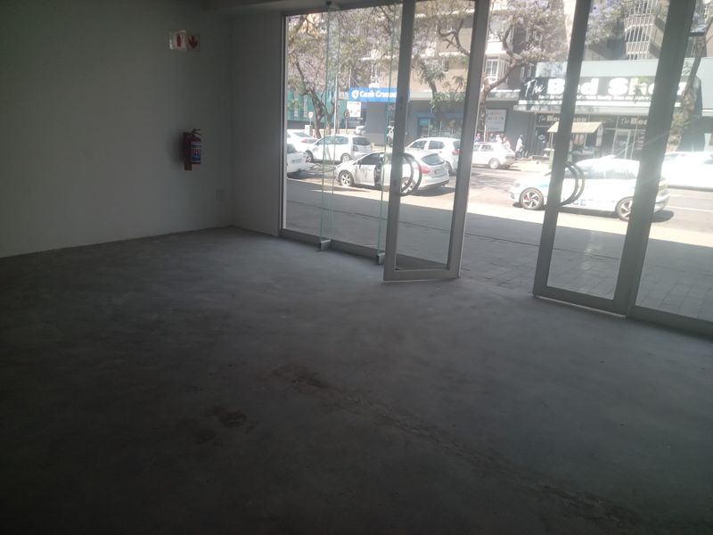 An empty retail space featuring large glass storefront windows, concrete flooring, and a wall-mounted fire extinguisher, offering high visibility to the street.
