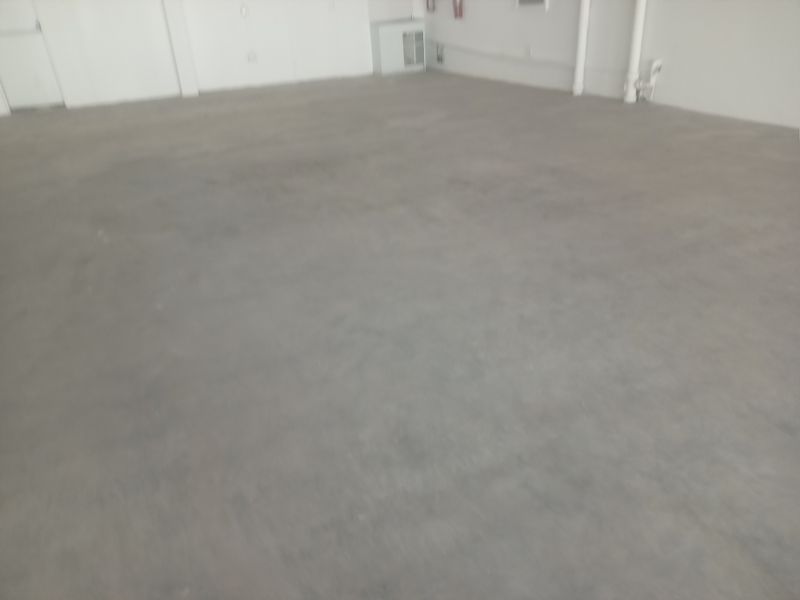 An open-plan retail space featuring unfinished concrete flooring, exposed white walls, and visible utility piping.